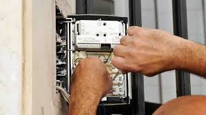 Technician installing a wall-mounted intercom system with audio and video capabilities for secure communication between building entry points.