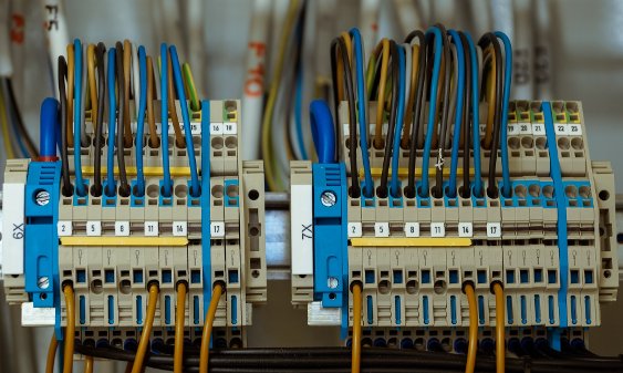 wiring-electric-network-cables-600-optimized Close-up of organized electrical wiring and terminal blocks in a control panel, showing blue, yellow, and black cables connected for power distribution.